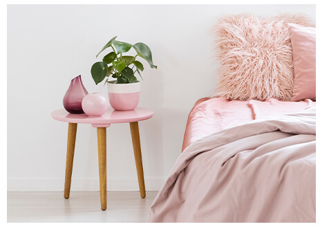 white and pink pastel coloured bedroom and pink and wooden bedside table  with plant on top